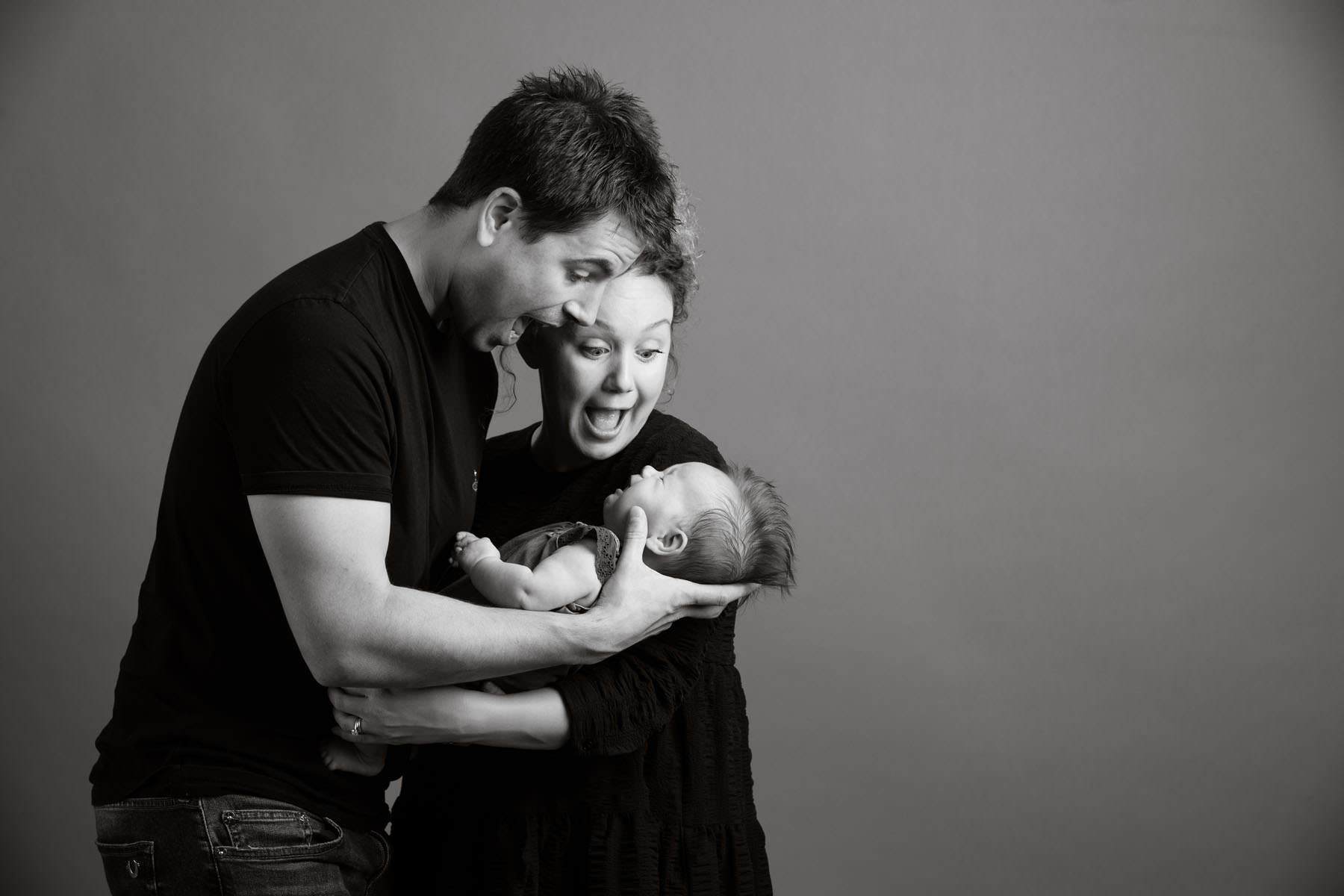 mum and dad making silly faces at an unhappy baby girl in their studio photoshoot